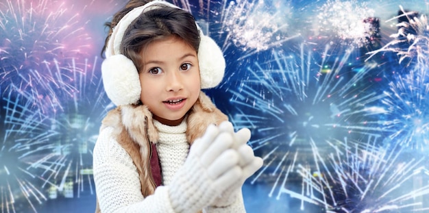 Inverno, vacanze, bambini e concetto di persone - bambina felice che indossa le cuffie su sfondo di fuochi d'artificio