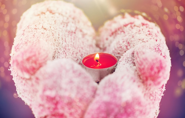 winter holidays, christmas and people concept - close up of hands in mittens holding burning tea candle outdoors