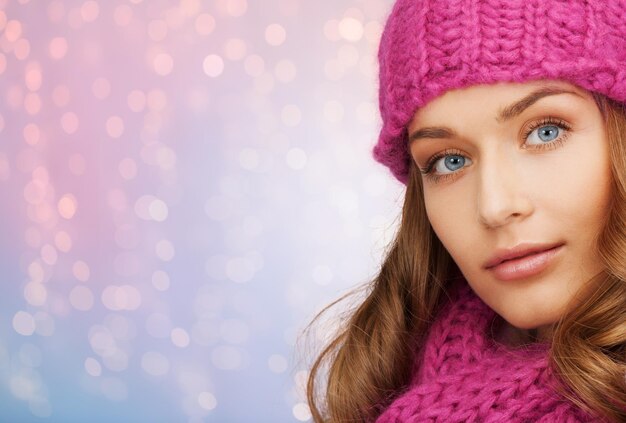 winter holidays, christmas and people concept - close up of young woman in hat and scarf over rose quartz and serenity lights background