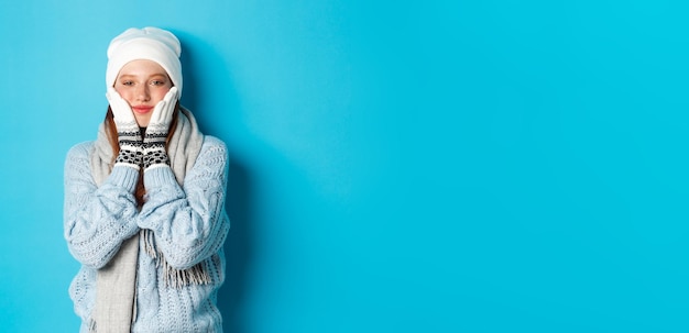 Photo winter and holidays concept cute girl in white beanie sweater and gloves squeezing cheeks and smilin