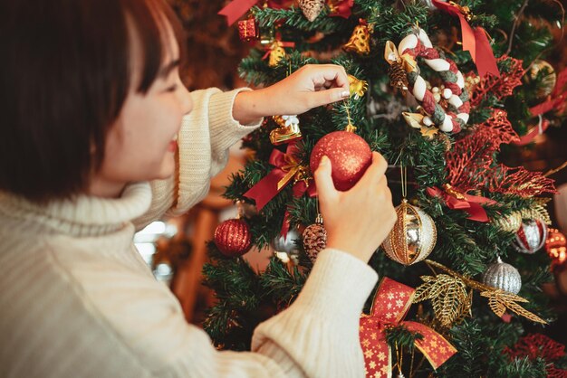 冬の休日のコンセプト、新年のお祝いのためにクリスマスツリーを飾る幸せな女性。