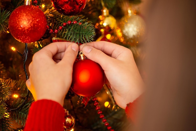 Vacanze invernali e concetto di decorazione mani di una ragazza che appende palla rossa sull'albero di natale colori caldi e atmosfera