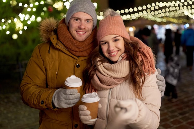 winter holidays, hot drinks and people concept - happy couple with coffee taking selfie in christmas evening