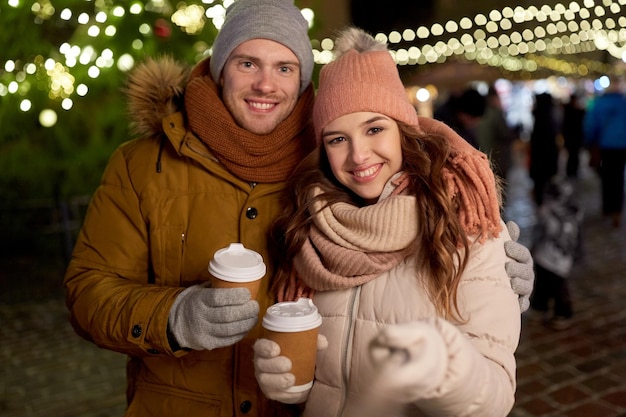 Photo winter holidays, hot drinks and people concept - happy couple with coffee taking selfie in christmas evening