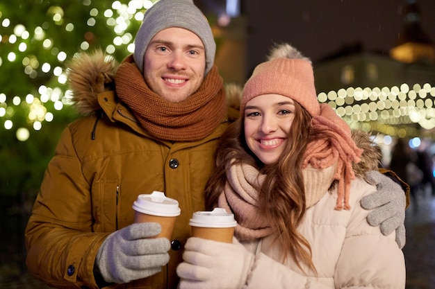 winter holidays, hot drinks and people concept - happy young couple with coffee at christmas market in evening