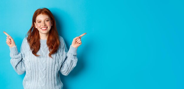 Winter holidays and people concept cute teen girl with red hair smiling and pointing fingers sideway