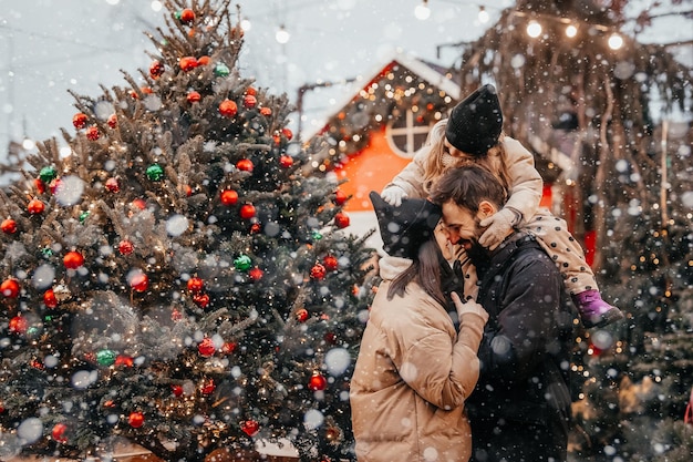 Winter holidays and people concept happy family with little daughter choosing Xmas tree at Christmas tree fair Happy preparation for the celebration of New Year holidays