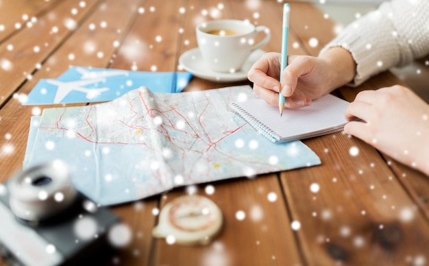 Фото Зимние каникулы, туризм, путешествия, направление и люди концепция - путешественник руки с картой и кофе писать в блокнот над снегом