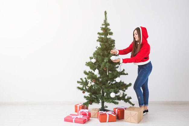 Winter holidays xmas and people concept beautiful young woman decorating a christmas tree in white