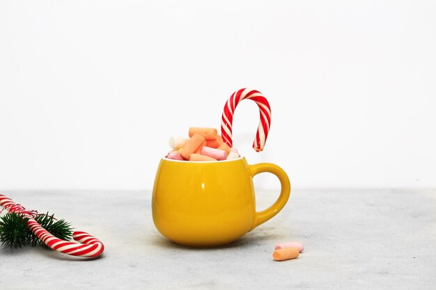 Photo winter hot drink in a yellow mug with multicolored marshmallows on a grey background festive decoration
