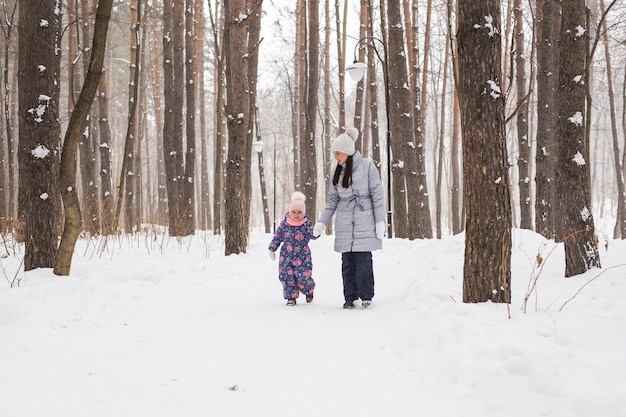 Winter, jeugd en mensen concept - moeder loopt met haar dochtertje in besneeuwde bossen