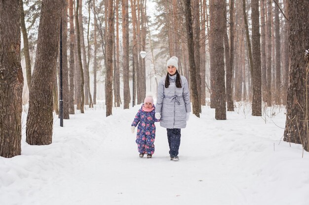 Winter, jeugd en mensen concept - moeder loopt met haar dochtertje in besneeuwde bossen