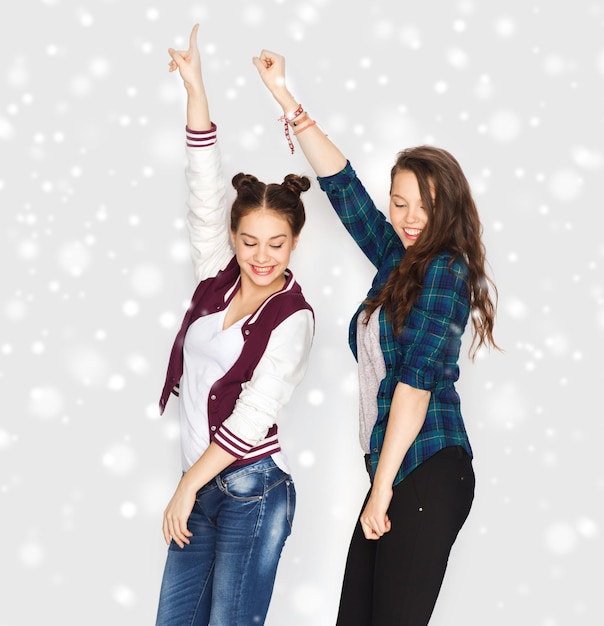 winter, kerstmis, mensen, tieners en feestdagen concept - gelukkig lachende mooie tienermeisjes of vrienden dansen over grijze achtergrond en sneeuw