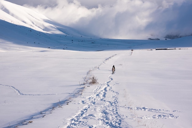 Winter landscape footprints path and people walking in snow valley in bright sunny day