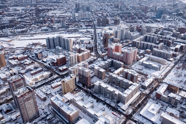 Photo winter landscape from a aerial view of the city of novosibirsk of the streets with a road tall buildings houses with roofs under white snow parking lots cars trees