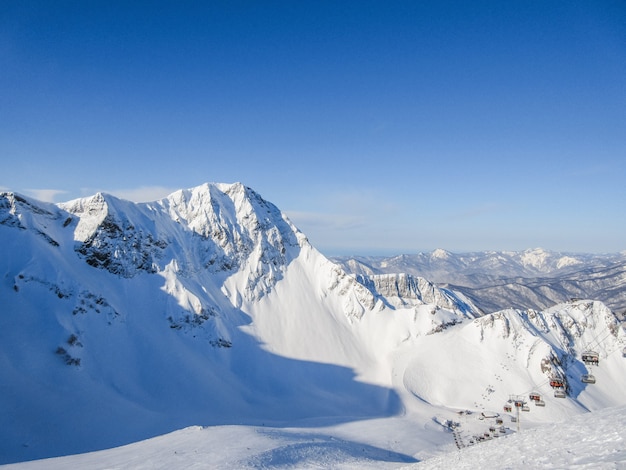 山の冬の風景です。山は晴れた冬の日に雪で覆われています