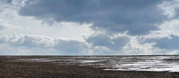 Winter landscape of plowed field, the ground is covered in places with a layer of snow and beautiful cloudly sky