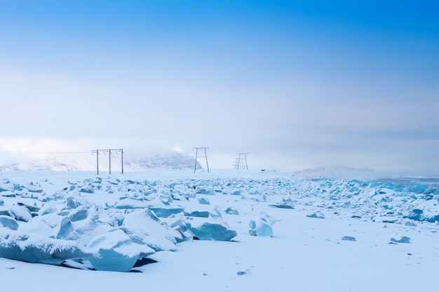 Winter landscape, power lines on a snowy field by the mountains, Iceland