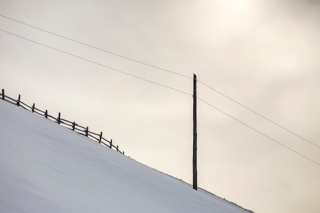 冬の風景。白い雪と明るい空のコピースペースに電流線と急な山の斜面。