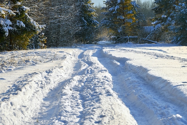 Winter landscape with a country road with very deep car tracks in the snow in sunny winter day