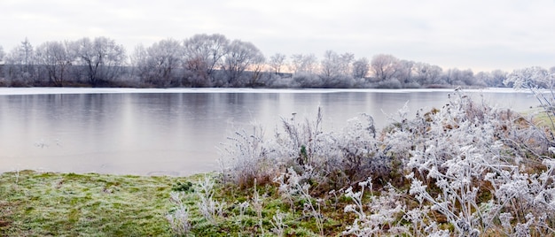 Paesaggio invernale con piante ricoperte di brina dal fiume e il riflesso degli alberi nell'acqua. giornata invernale, panorama