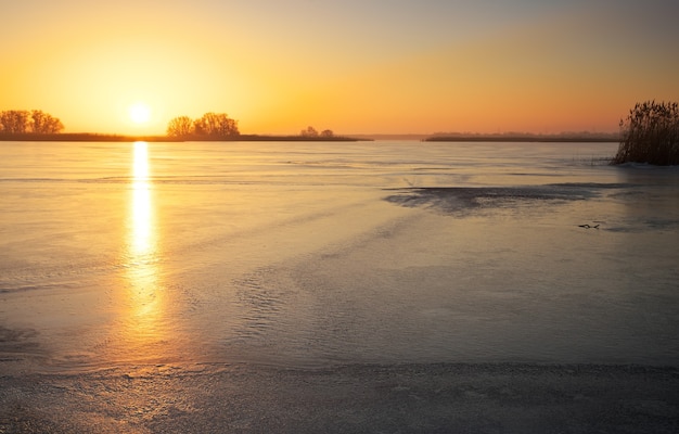 Winter landscape with frozen lake and sunset fiery sky. Composition of nature.