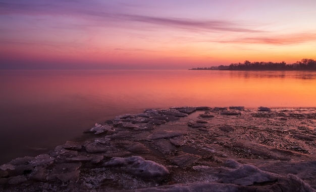 Winter landscape with frozen lake and sunset sky. Composition of nature.