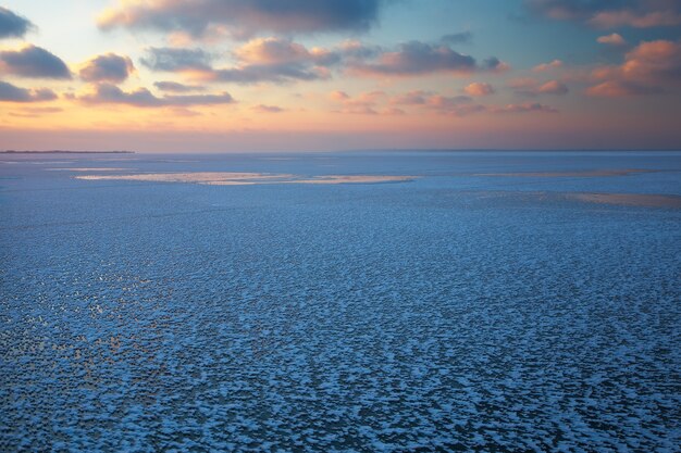 Winter landscape with frozen lake and sunset sky.