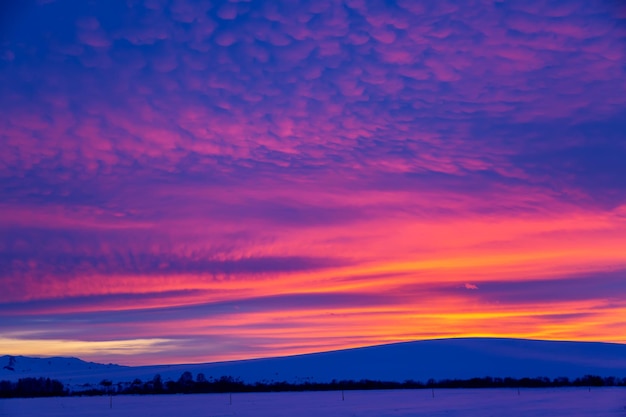 Foto paesaggio invernale con montagne durante un incredibile cielo al tramonto saturo vivido nei colori rosa, viola e blu. sfondo del tramonto.