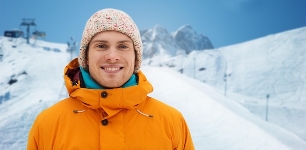 winter, leisure, clothing and people concept - happy teenage boy or young man in winter clothes over downhill skiing and mountains background