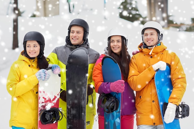 winter, leisure, extreme sport, friendship and people concept - happy friends in helmets with snowboards