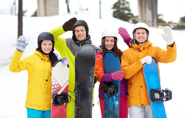 winter, leisure, extreme sport, friendship and people concept - happy friends in helmets with snowboards