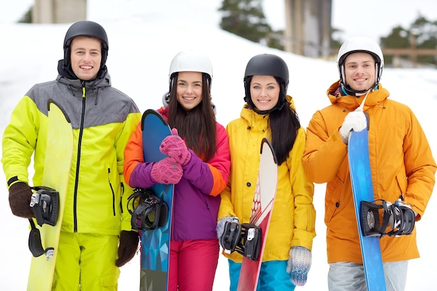 winter, leisure, extreme sport, friendship and people concept - happy friends in helmets with snowboards