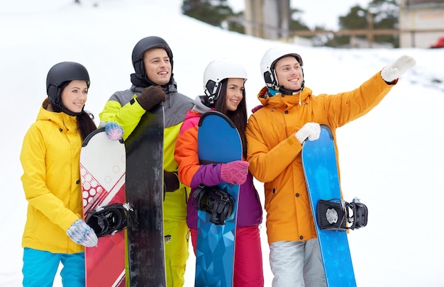 winter, leisure, extreme sport, friendship and people concept - happy friends in helmets with snowboards