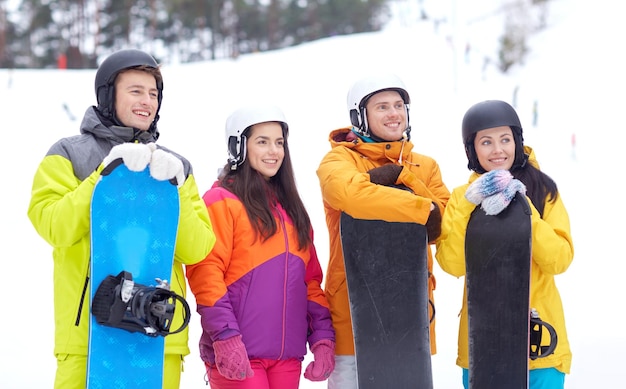 winter, leisure, extreme sport, friendship and people concept - happy friends in helmets with snowboards