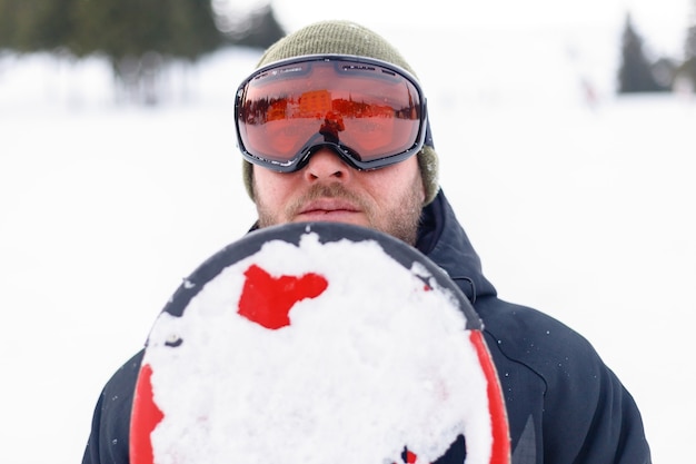 冬、レジャー、スポーツ、人々のコンセプト-山でスノーボードをする男性。青い空を背景に山の頂上で休んでいるスノーボーダー。スキーリゾート。