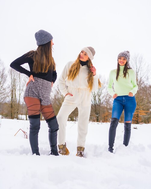 Photo winter lifestyle, three caucasian friends with winter outfit and wool hats enjoying the snow next to snowy pine trees, holidays in nature