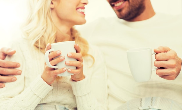 winter, love, family and happiness concept - close up of happy couple with tea cups at home