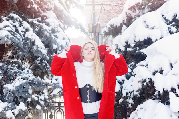 Winter, mode, mensen concept - mode Portret van een mooie jonge vrouw loopt rond de stad glimlachend rode bontjas close-up sneeuwvlokken koude winter, frisse lucht inademen bij vorst winterdag. zonsondergang