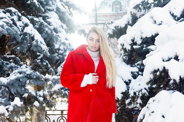 Winter, mode, mensen concept - mode Portret van een mooie jonge vrouw loopt rond de stad glimlachend rode bontjas close-up sneeuwvlokken koude winter, frisse lucht inademen bij vorst winterdag. zonsondergang