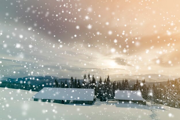 Winter mountain landscape. Old wooden houses on snowy clearing on background of mountain ridge, spruce forest and cloudy sky. Happy New Year and Merry Christmas card.