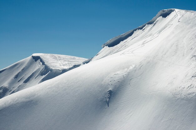 Фото Зимний горный хребет с нависающими снежными шапками и трассами для сноуборда на голубом небе