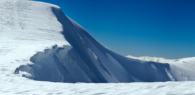 Winter mountains ridge with overhang snow caps on blue sky