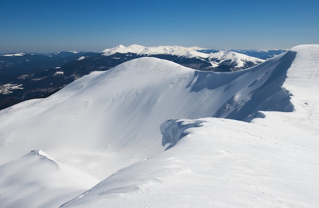 Winter mountains ridge with overhang snow caps and snowboard tracks on blue sky