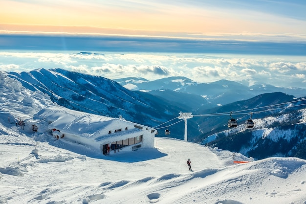 Winter mountains. Snow-capped peaks and fog in the valleys. Blue and pink sky over the ski run. Ski lift and bar