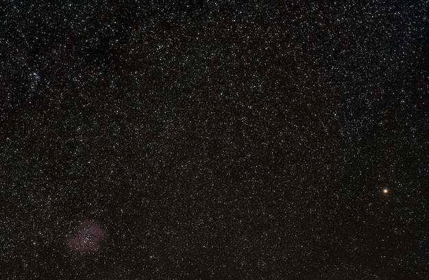 Winter night sky with many stars, Rosette nebula visible in lower left corner,  bright yellow Betelgeuse star on right side