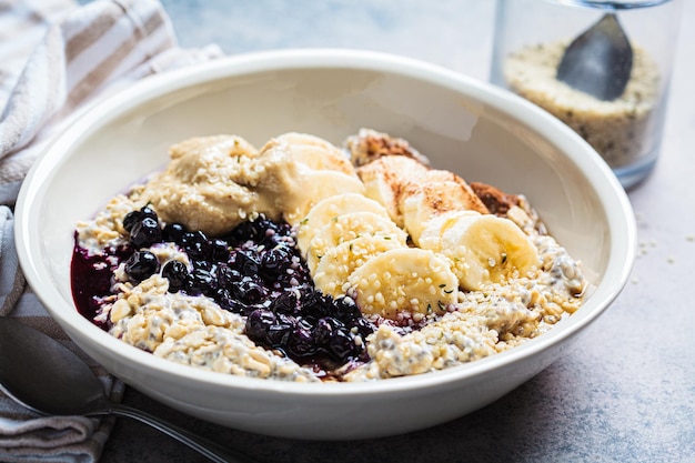 Foto winter ontbijt concept overnachting havermout met banaan berry chia zaden sesam tahini kaneel en siroop in een kom donkere achtergrond