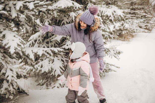 Winter outdoor recreation. Happy mother shakes off snow from a branch on a child standing among snow-covered fir trees