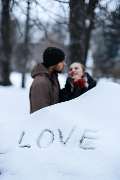 Winter outdoors portrait of young couple in love and word love on snow valentines day outdoors