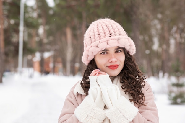 Winter portrait of an cute brunette woman wears pink knitted hat and coat walking in the forest.  Empty space